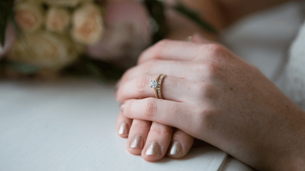 a bride’s hand wearing a wedding ring and an engagement ring