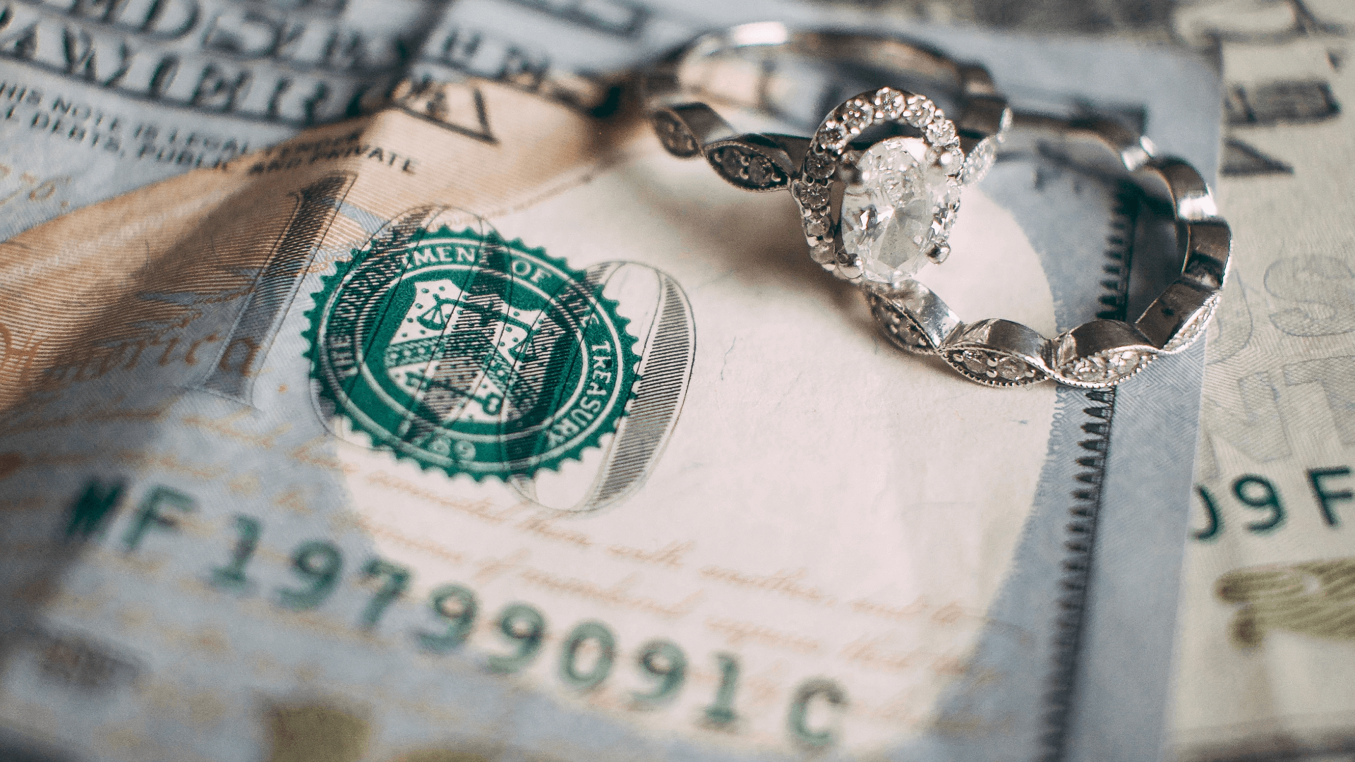 a diamond engagement ring sits on top of dollar bills
