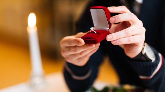 a man holds a red velvet box with an engagement ring inside
