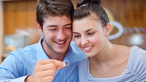 a couple tries to pick a wedding band at a jewelry store