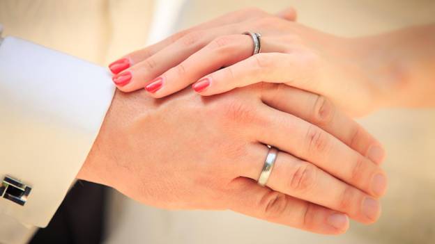 a close-up of a  bride and groom’s hands wearing wedding rings