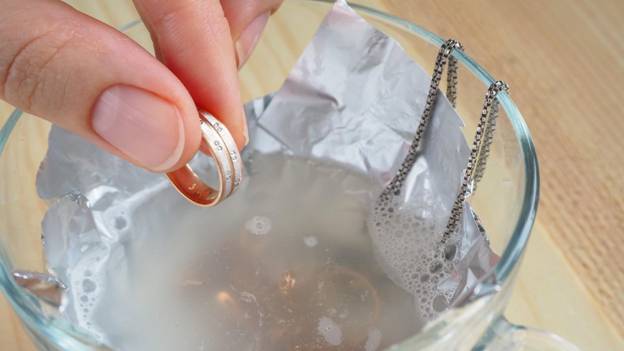 a person is cleaning jewelry in a cup of water