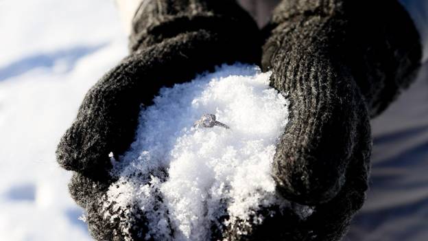 gloved hands hold an engagement ring in a pile of snow