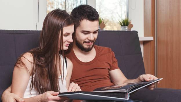 a couple looks through a photo album while sitting on a couch