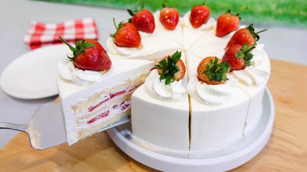 a person cuts a cake with whipped cream and strawberry fruits against a wood table background