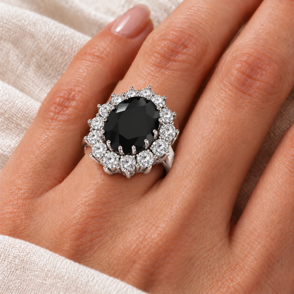 AD4841 natural 12x10mm oval black diamond and fourteen diamond halo ring in 14k white gold, ivory-linen closeup with the ring aligned at the base of the left ring finger