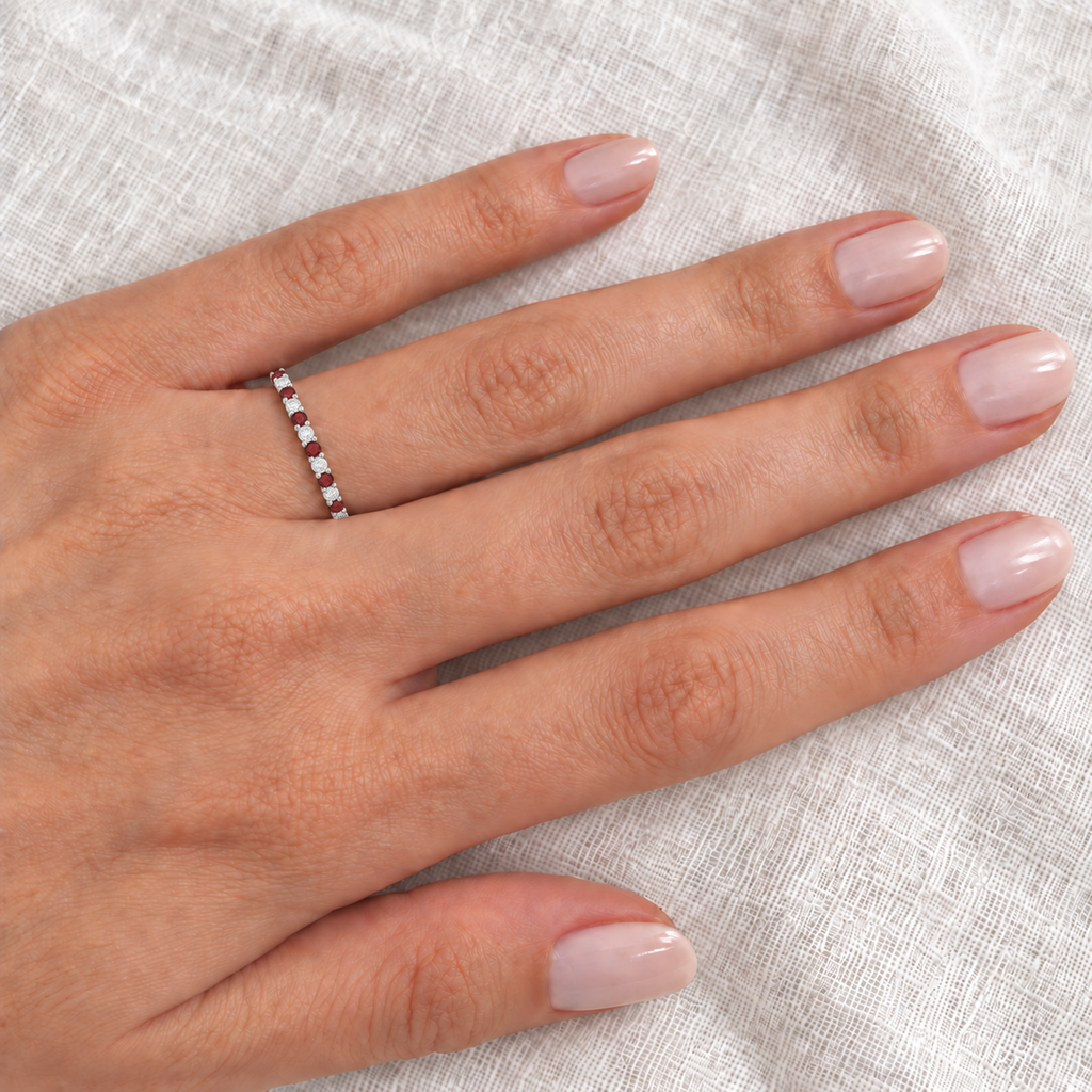 14k white gold garnet and diamond eternity band on left ring finger, closeup on ivory linen