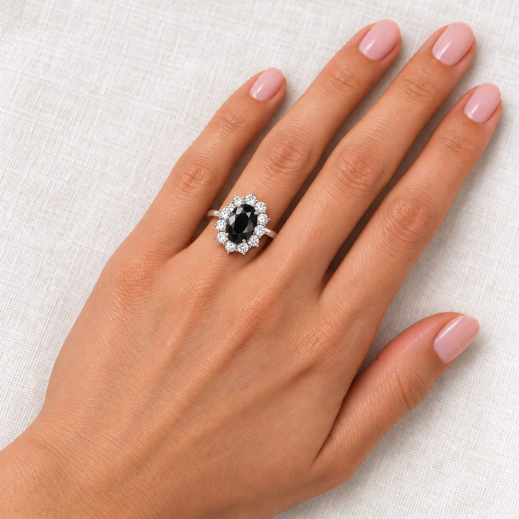 9x7mm oval Natural black diamond and twelve colorless diamond halo ring in 18k white gold at base of left ring finger aligned toward fingertip, ivory linen closeup