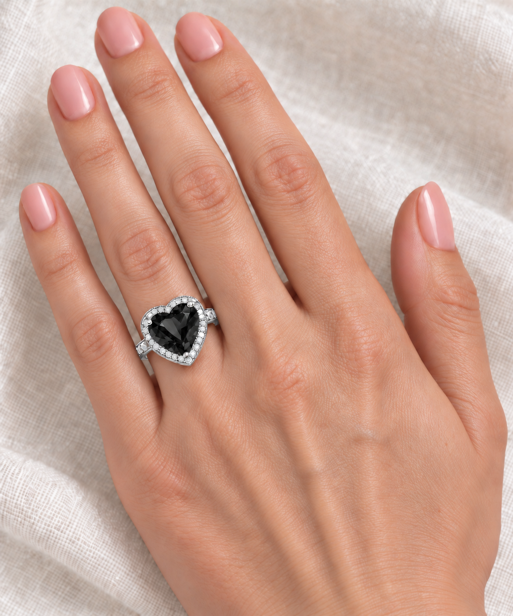 12x12mm heart-shaped lab black diamond and white diamond halo ring in 14k white gold, 5.41ct — correctly scaled at base of left ring finger on ivory linen