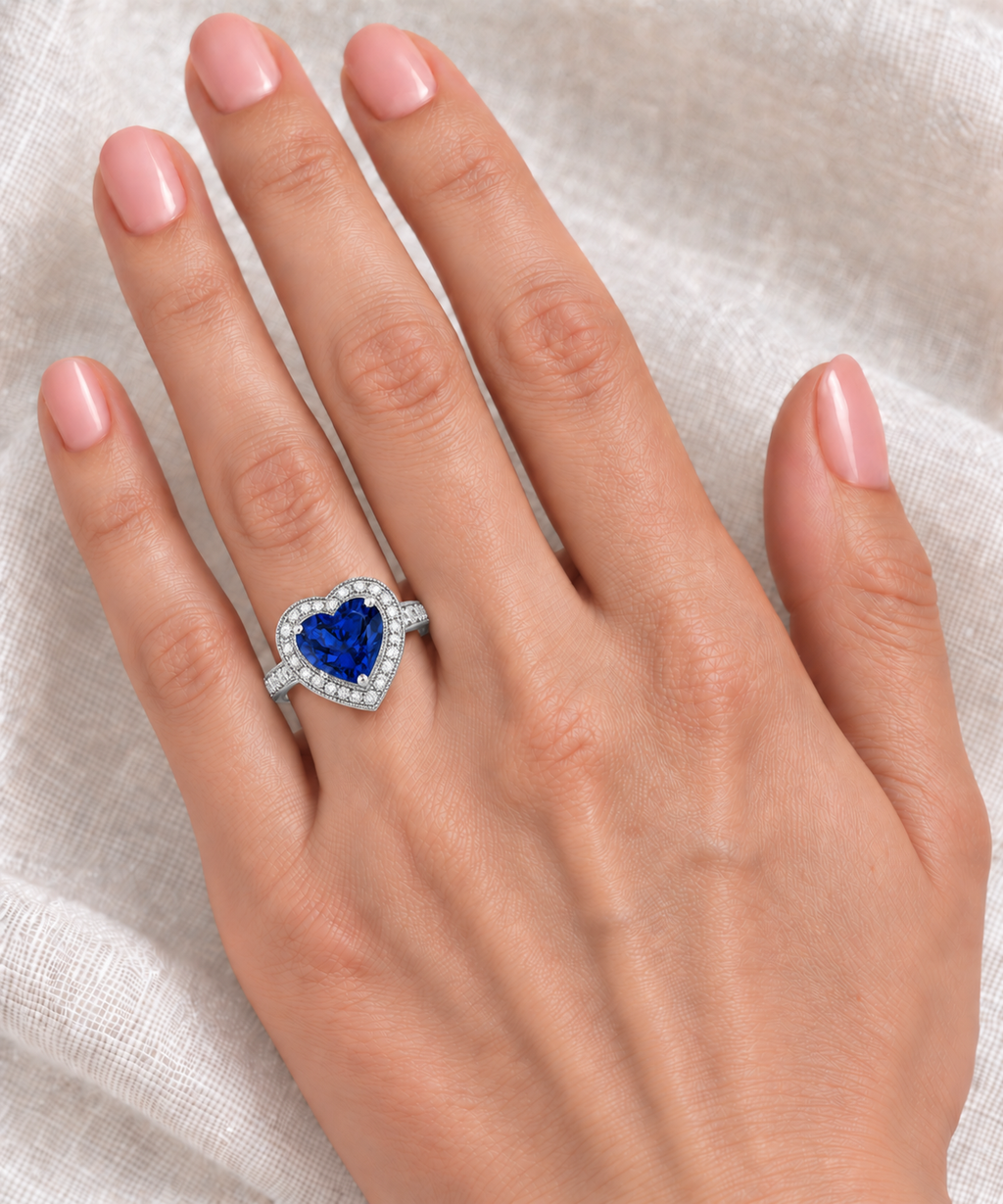 10x10mm heart-shaped lab blue sapphire and white diamond halo ring in 14k white gold, 3.66ct — correctly scaled at base of left ring finger on ivory linen