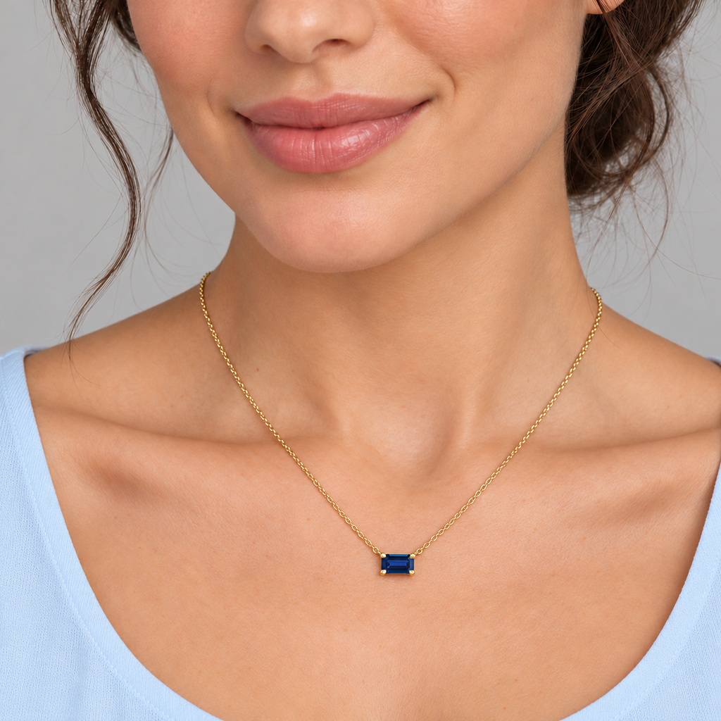 AZ29487 — close-up model wearing 5 × 3 mm emerald-cut lab-grown blue sapphire solitaire necklace in 14K yellow gold on an 18-inch cable chain; illustrative scale.
