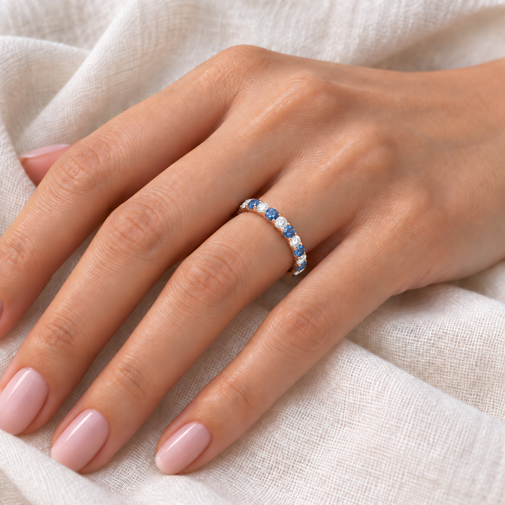 Lab blue and lab white diamond eternity band in 14k rose gold on left hand, ivory linen closeup