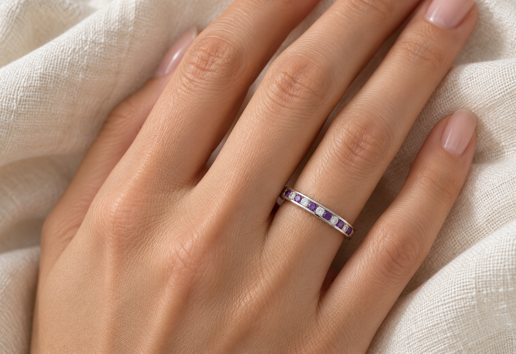 Channel set natural amethyst and diamond wedding band in 14k white gold on left hand over ivory linen