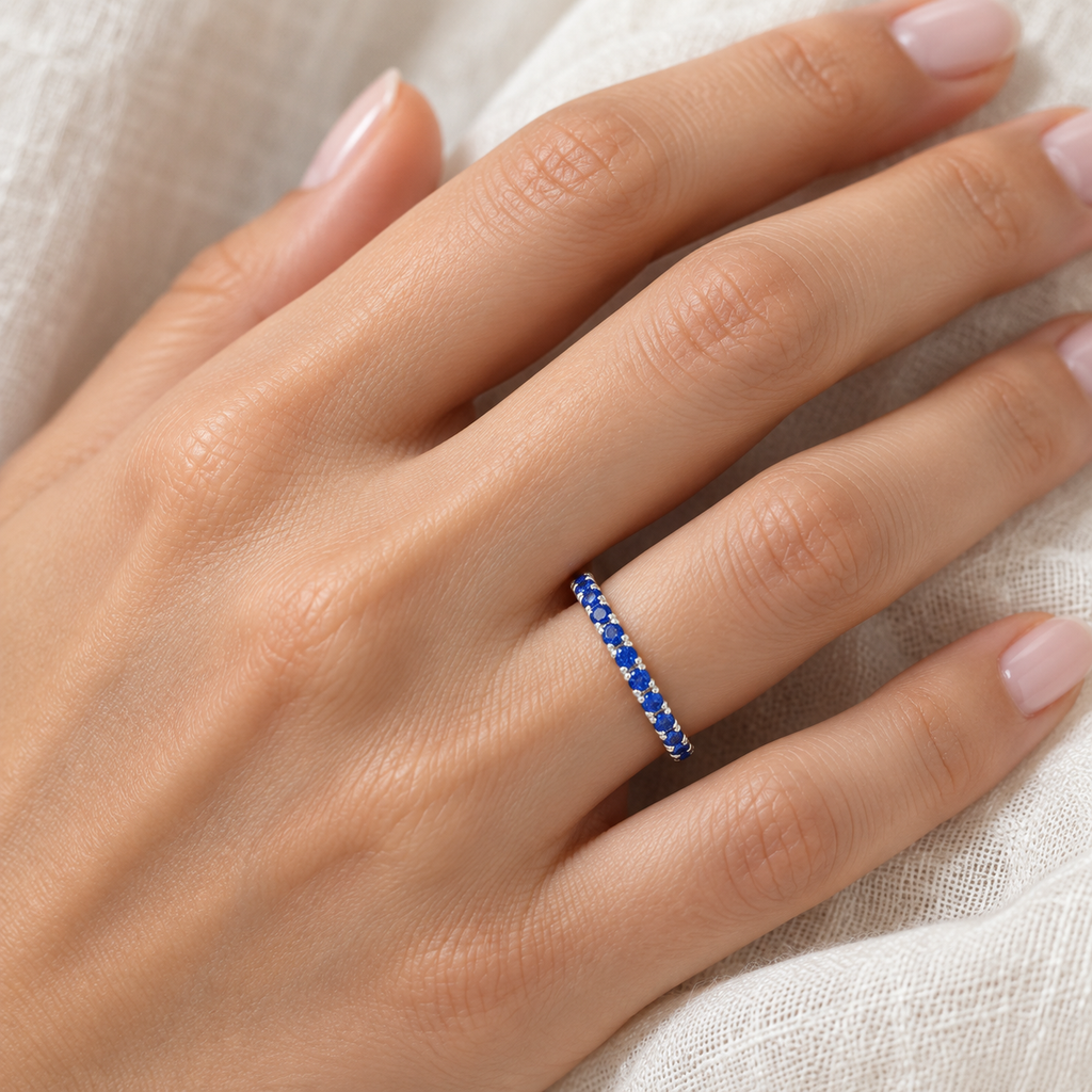 Blue sapphire palladium eternity band on left hand, close-up on ivory linen
