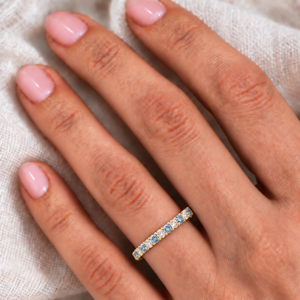 Lab-grown aquamarine and lab-grown diamond 3mm eternity ring band in 14k yellow gold on left ring finger, ivory linen closeup