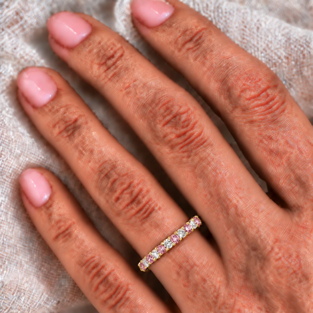 Lab-grown pastel pink sapphire and lab-grown diamond 3mm eternity ring band in 14k yellow gold on the left ring finger against ivory linen