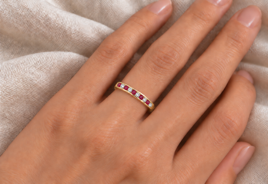 Ruby and diamond yellow gold channel ring on left hand over ivory linen