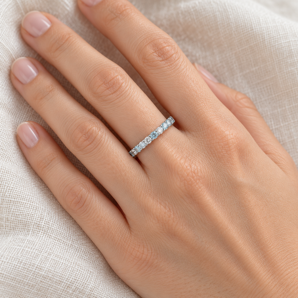 Aquamarine and diamond 14K white gold eternity band on left hand, close-up on ivory linen