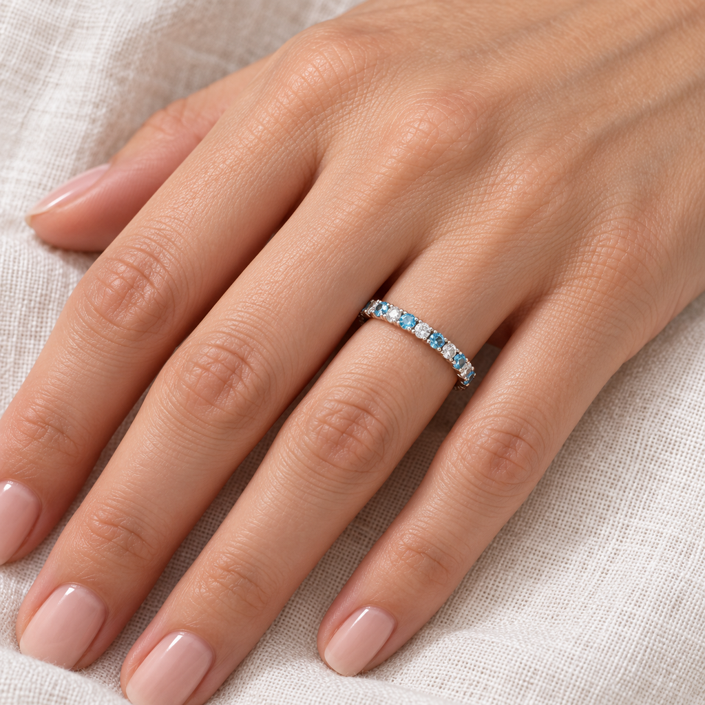 Blue topaz and diamond 14K white gold eternity band on left hand, close-up on ivory linen