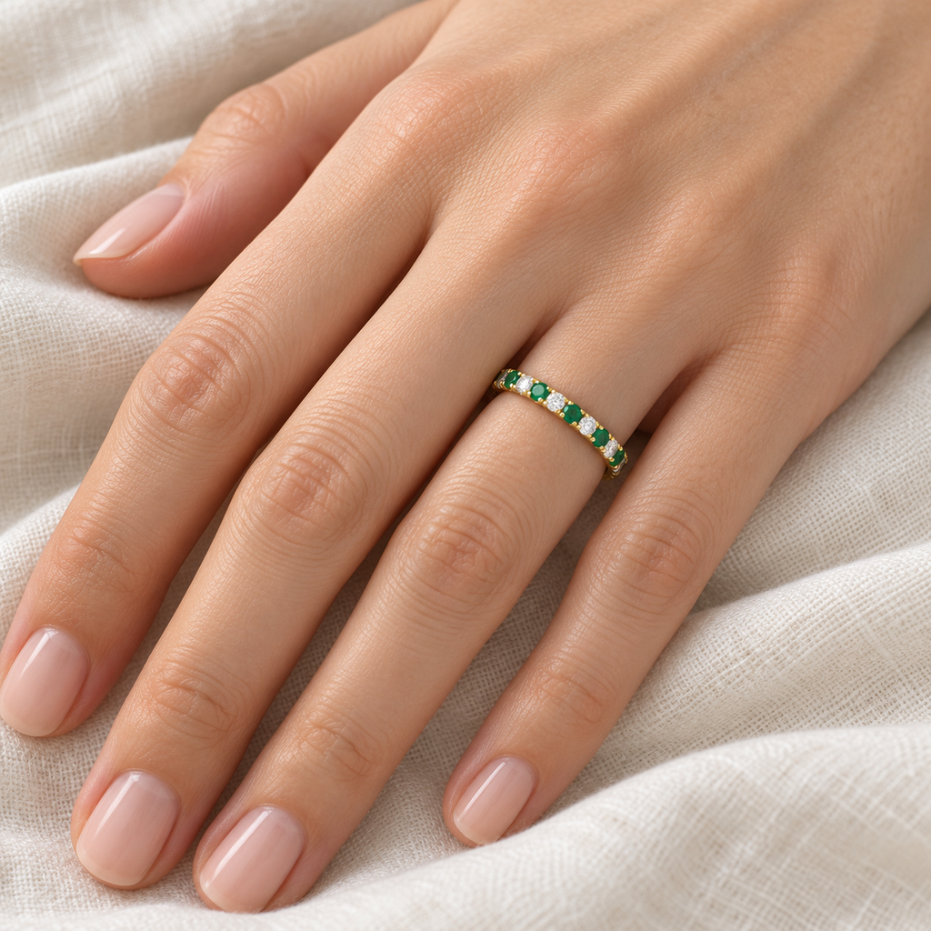Lab-grown emerald and lab-grown diamond 14K yellow gold 2 mm eternity band on left hand, ivory linen closeup