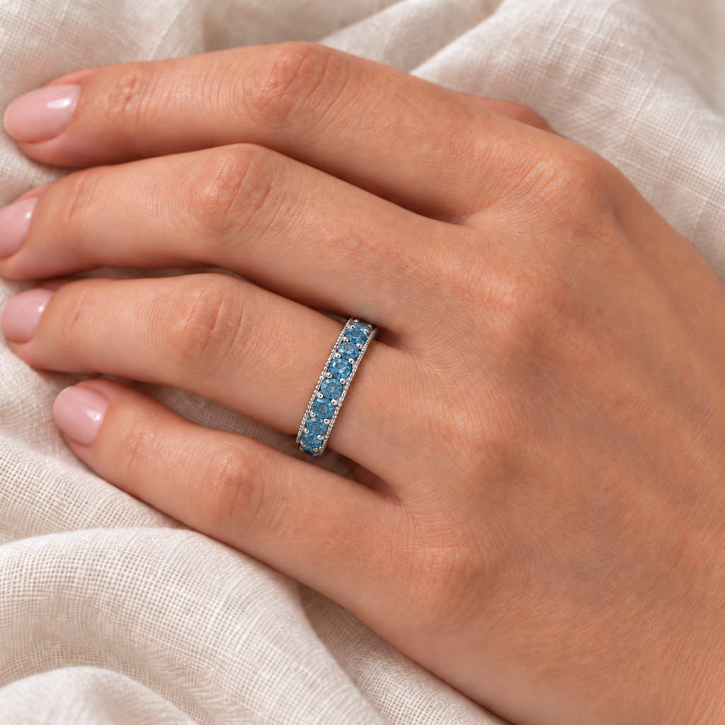 Fancy blue diamond white gold eternity ring on left hand over ivory linen