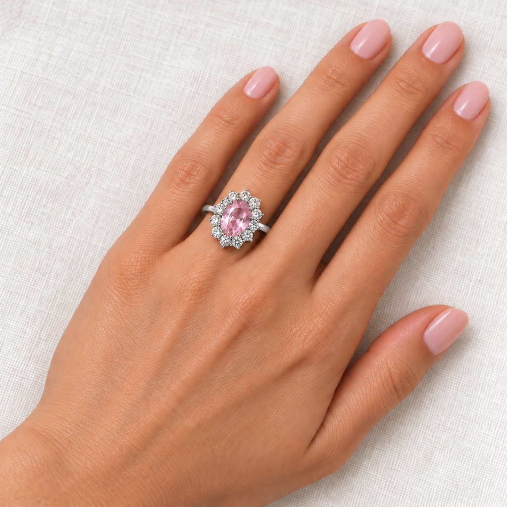 Oval natural pink sapphire and twelve diamond halo ring in 14k white gold worn on the left ring finger, with natural diamond reflections
