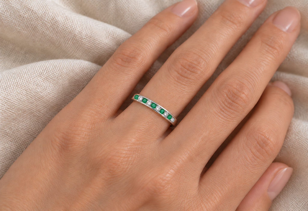 Alternating natural emerald and diamond channel-set ring in 14K white gold on left hand, ivory linen closeup