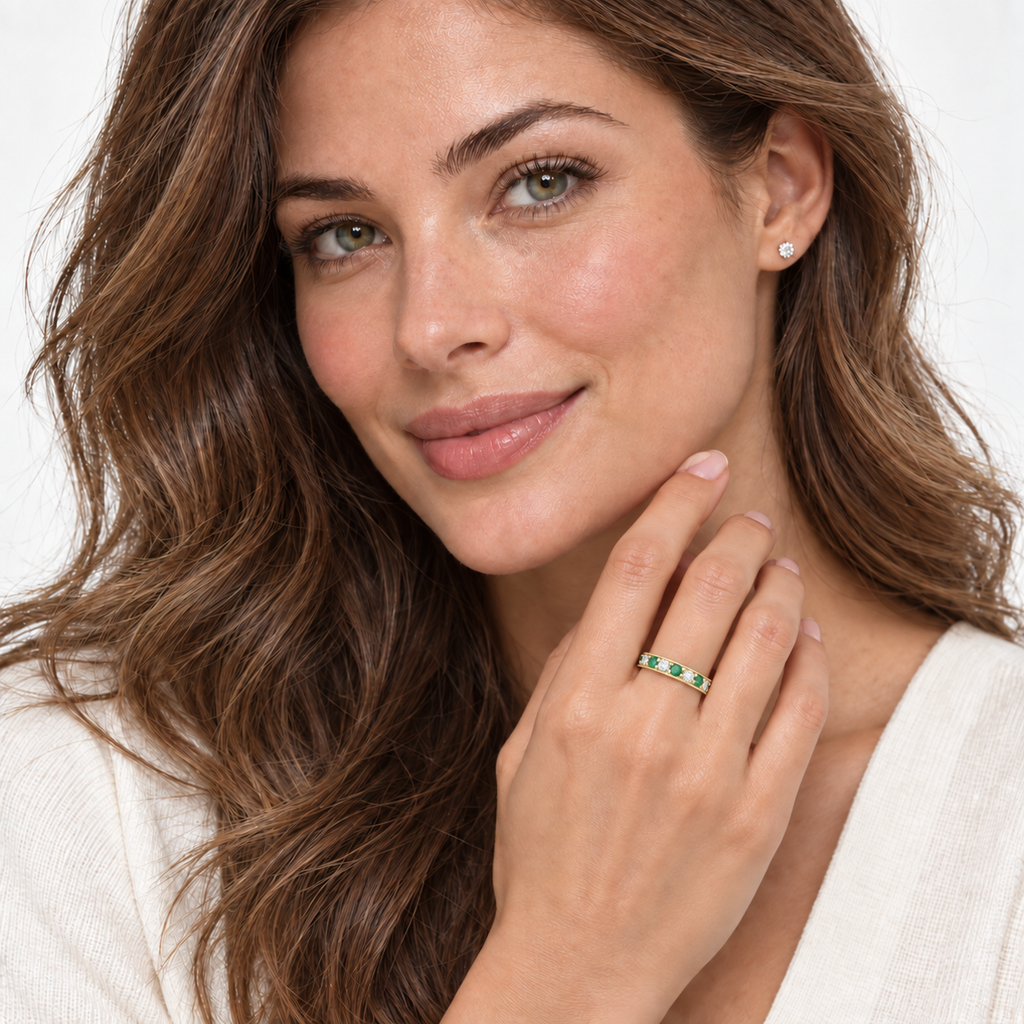 Emerald and diamond 3mm yellow gold band worn on left ring finger in studio portrait