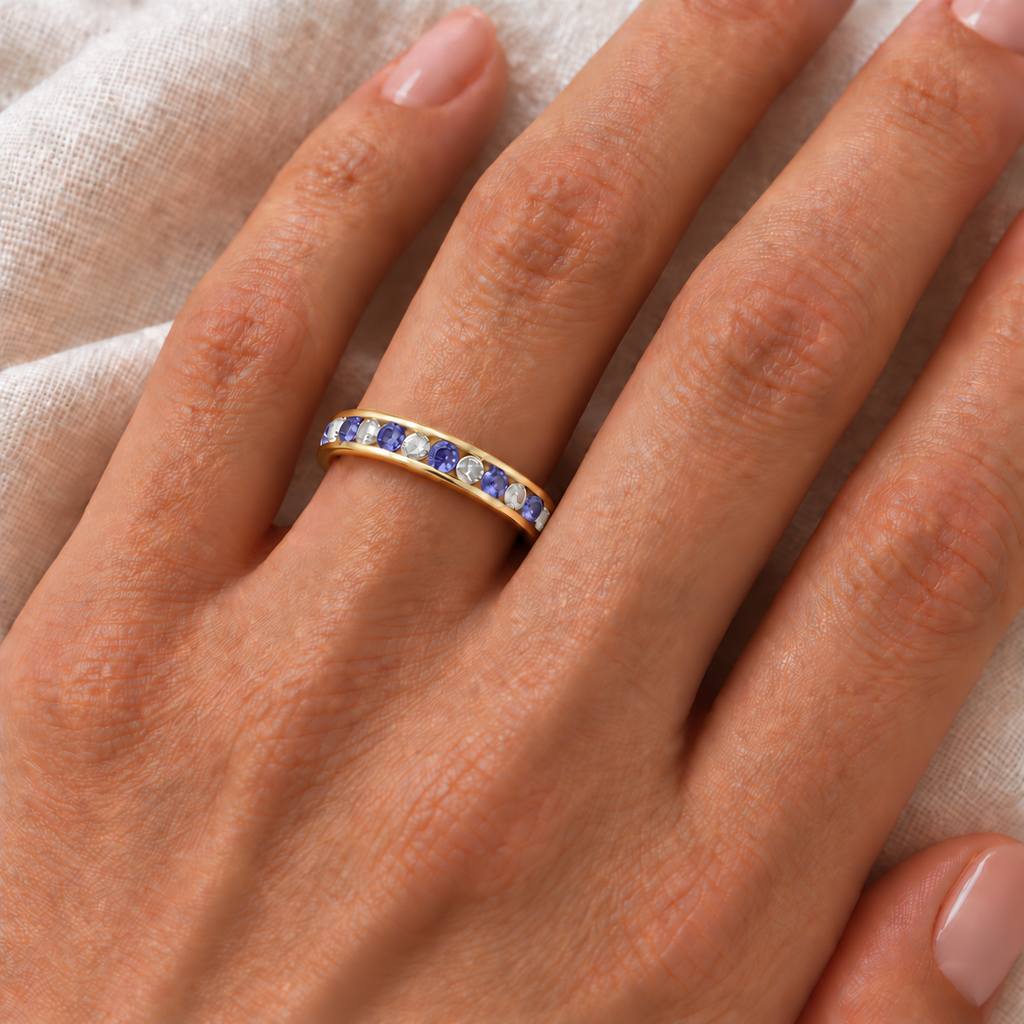 Tanzanite and diamond alternating channel-set eternity band in 14k yellow gold on left ring finger, ivory linen closeup