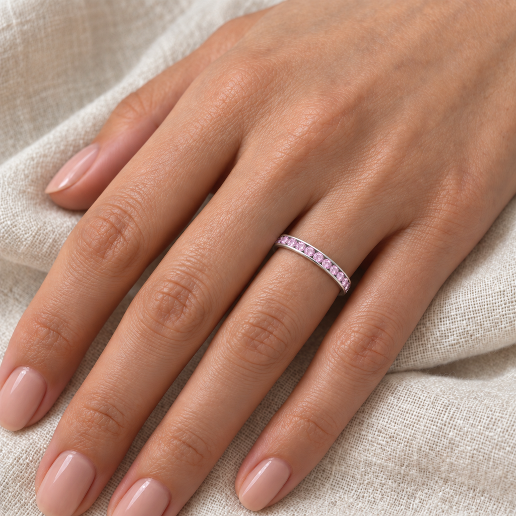 Pink sapphire channel band in 14k white gold, 3mm, 0.40ct — left ring finger closeup on ivory linen