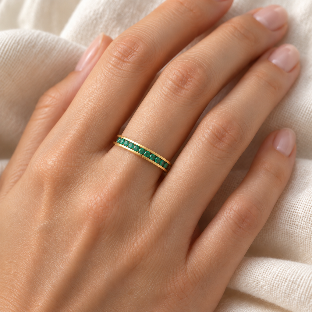 Fine 3 mm channel-set natural emerald band in yellow gold on left ring finger over ivory linen