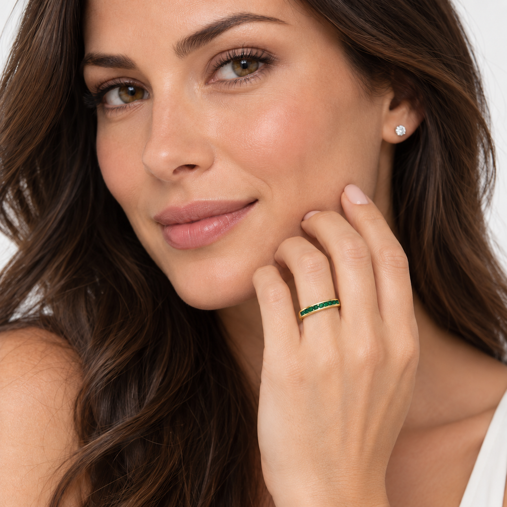 Fine 3 mm channel-set natural emerald band in yellow gold on left ring finger in studio portrait