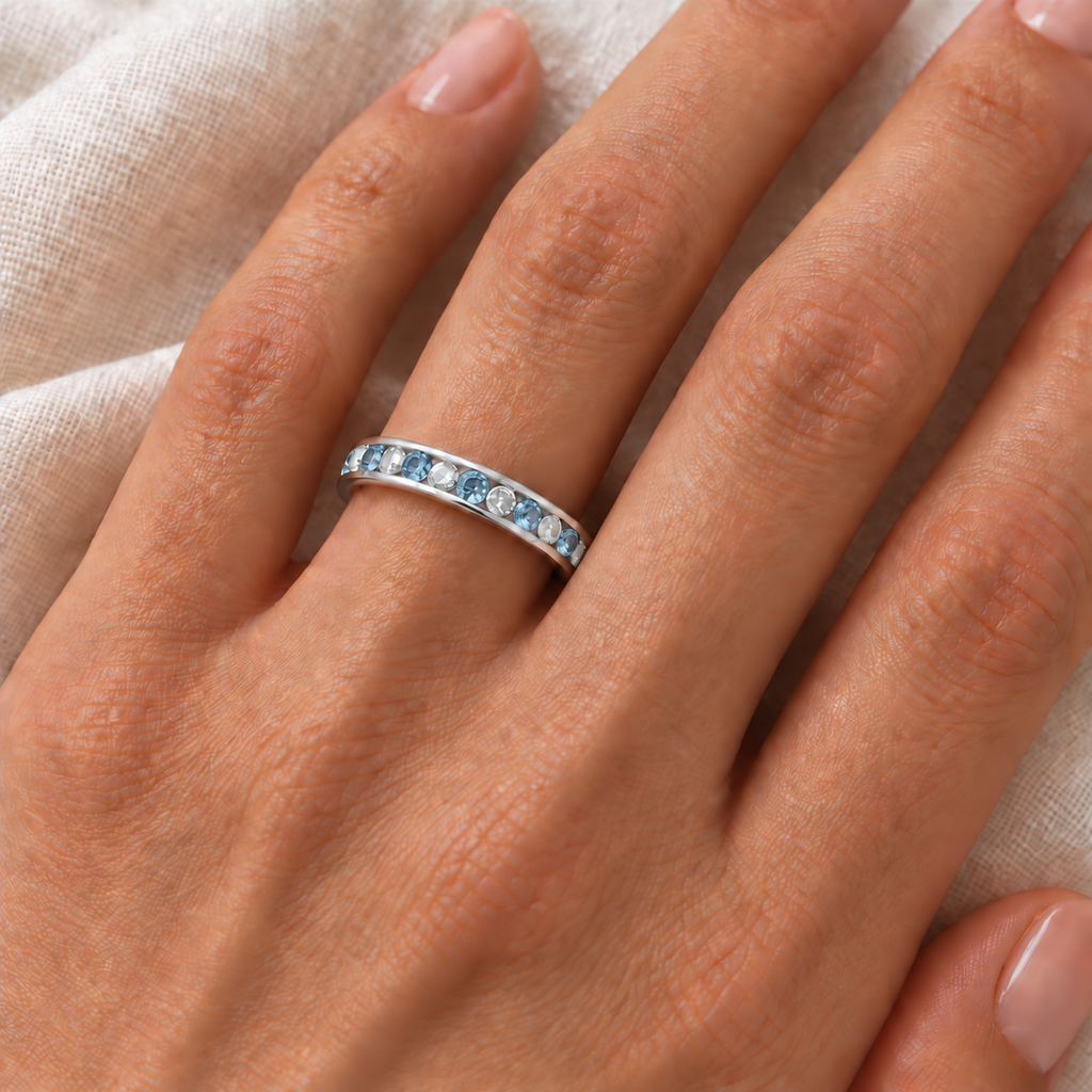 Blue topaz and diamond alternating channel-set eternity band in 14k white gold on left ring finger, ivory linen closeup