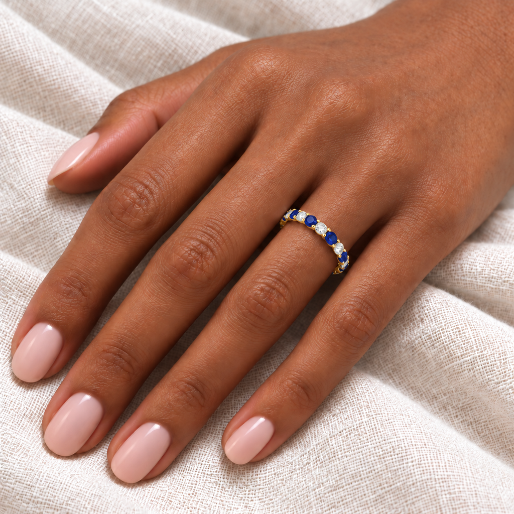 Blue sapphire and diamond eternity ring on hand, ivory linen close-up