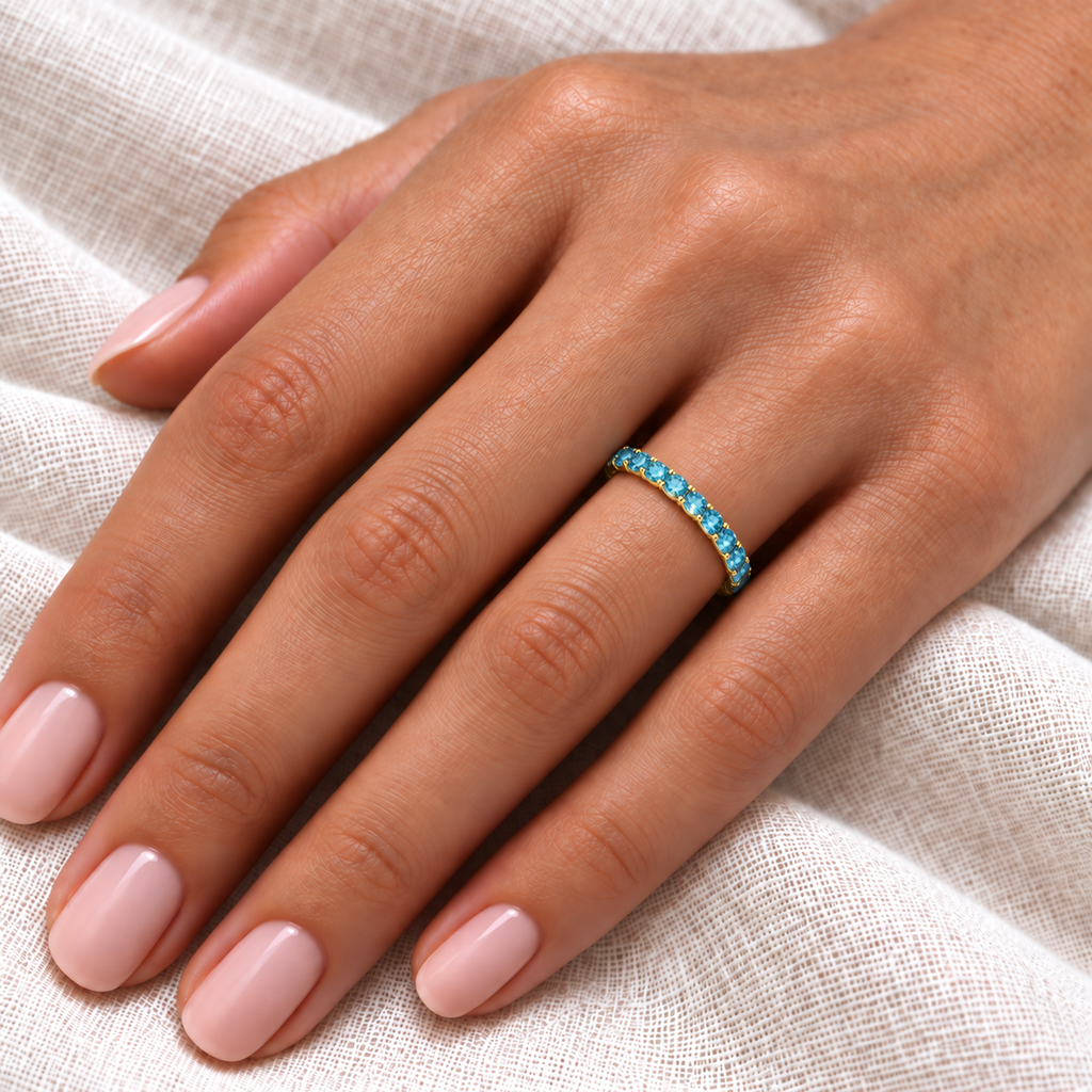 IR541LG fancy blue lab-grown diamond eternity band in 14k yellow gold, fine 2.5 mm close-up on the left ring finger over ivory linen