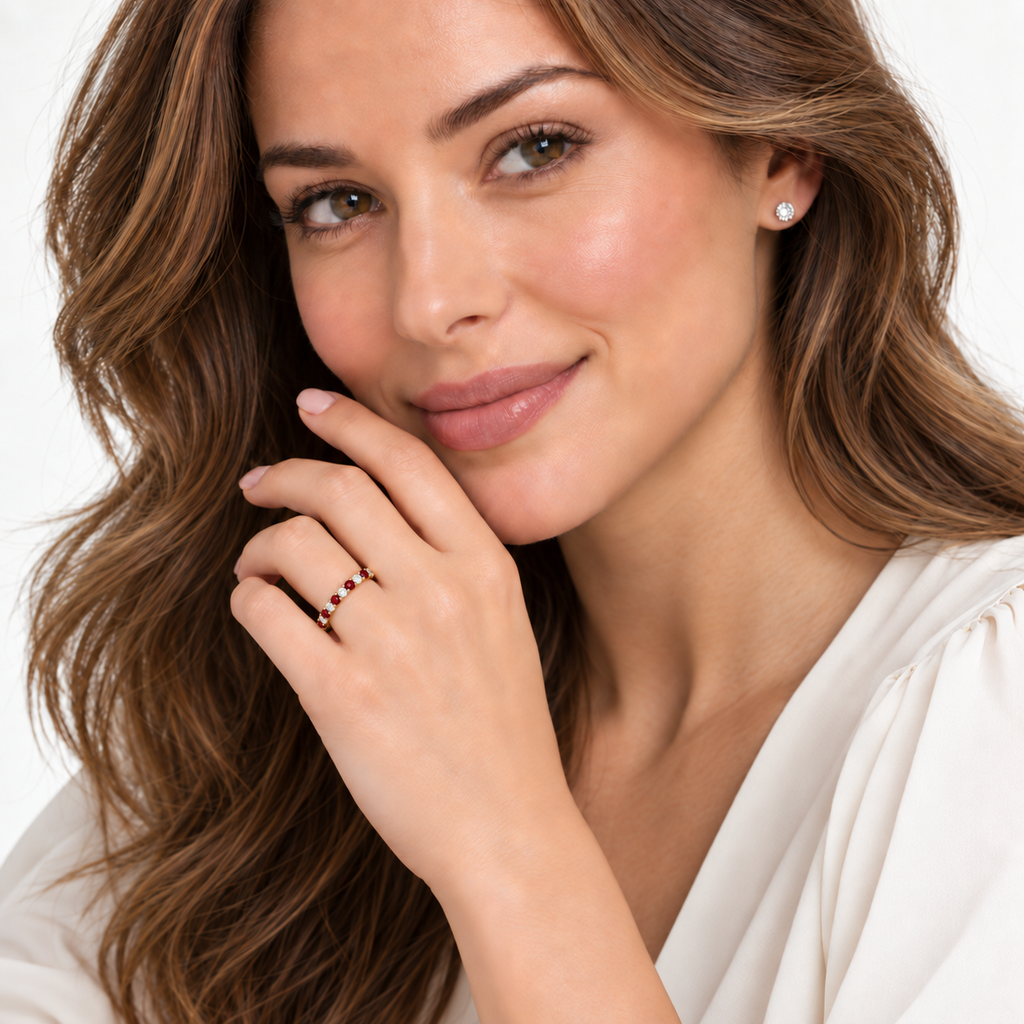 Lab-grown red garnet and lab-grown diamond eternity ring in 14k yellow gold, correctly scaled 2.5 mm alternating band, worn at the base of the left ring finger in a near-white studio portrait