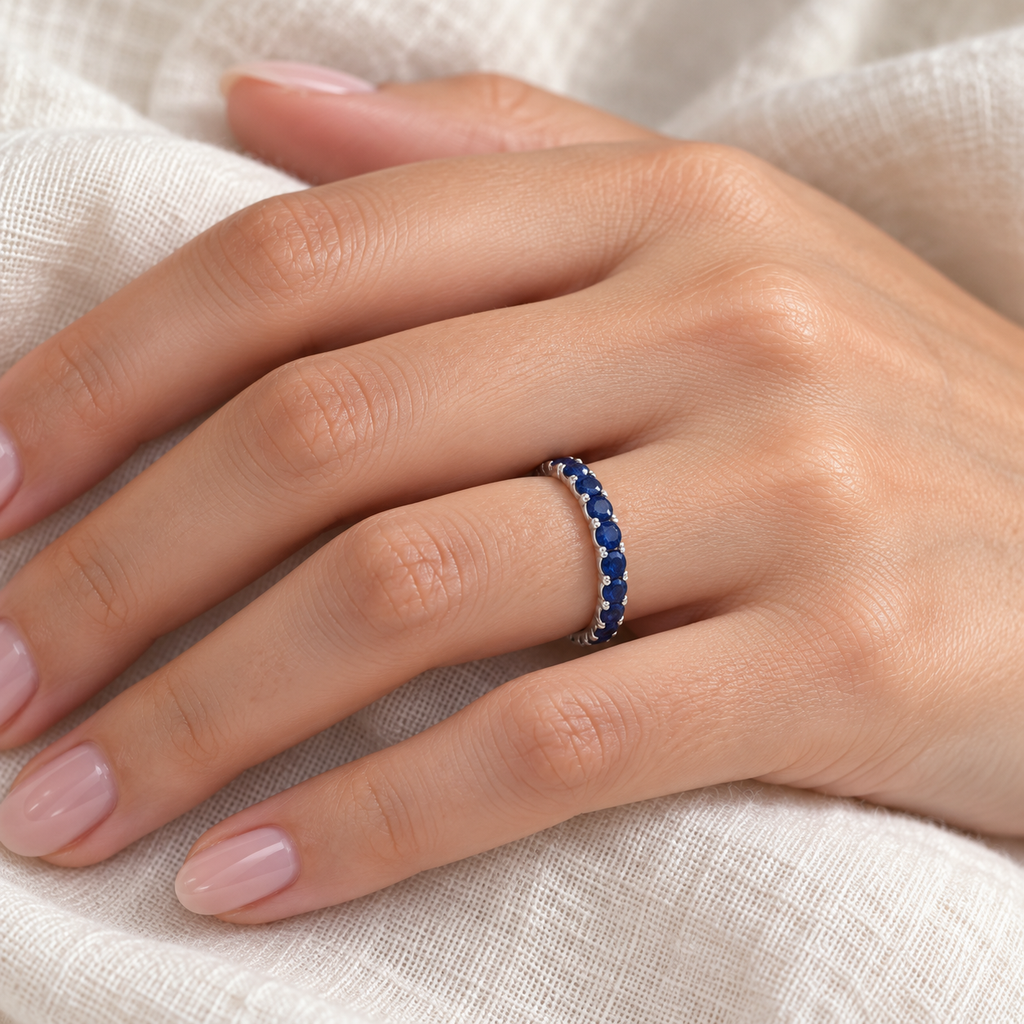 Blue sapphire 14K white gold eternity band on left hand, close-up on ivory linen