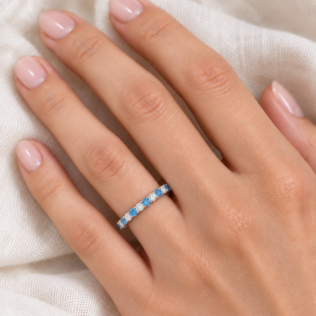 Lab blue topaz and lab diamond eternity ring in 14k white gold worn on hand at realistic 2.5 mm scale on ivory linen