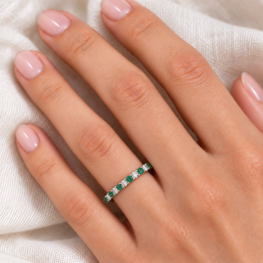Lab emerald and lab diamond eternity ring in 14k white gold worn at realistic 2.5 mm scale on the left hand over soft ivory linen