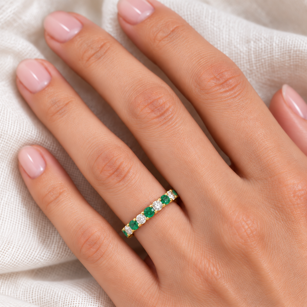 Emerald and diamond eternity ring in 14k yellow gold worn on hand over soft ivory linen