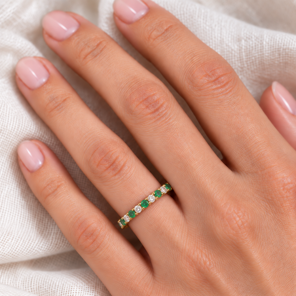Lab emerald and lab diamond eternity ring in 14k yellow gold worn at realistic 2.5 mm scale on the left hand over soft ivory linen