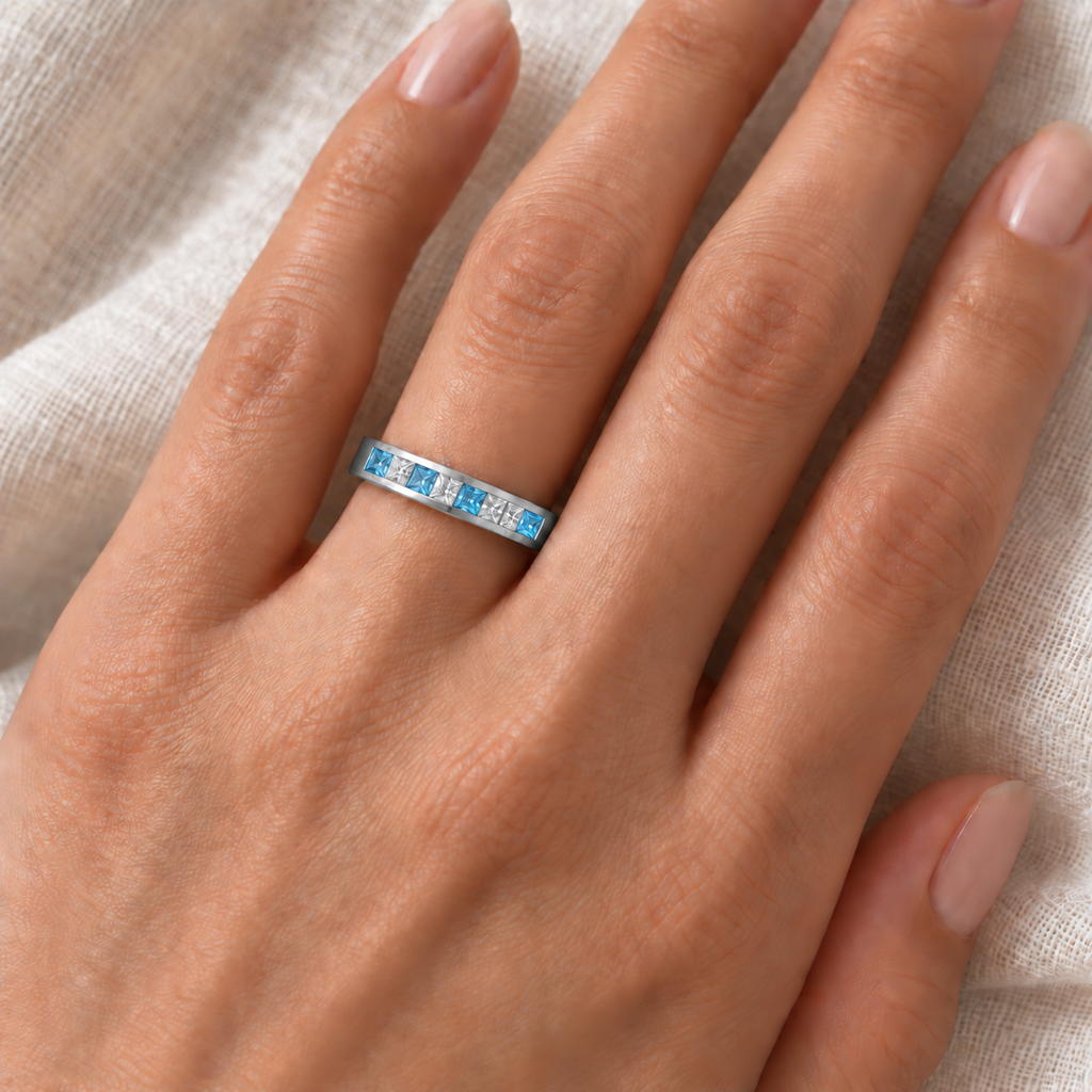 Princess-cut blue topaz and diamond channel ring in 14K white gold on left ring finger over ivory linen