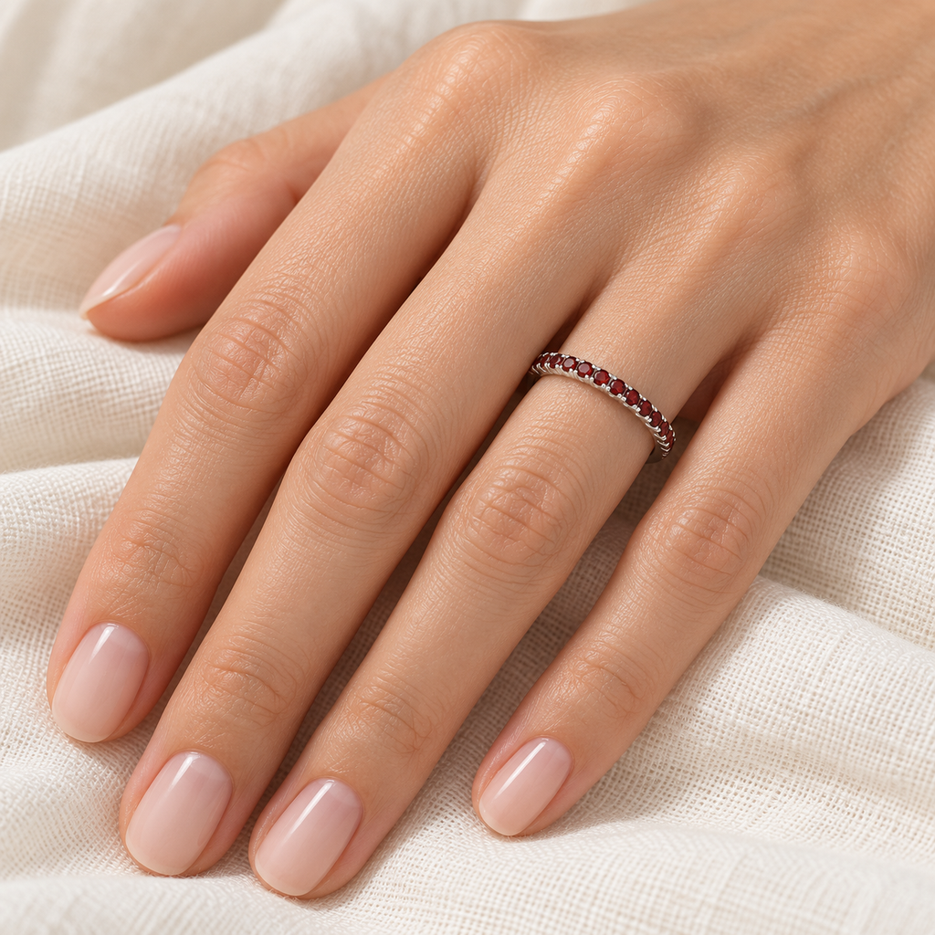 Thin natural garnet half-eternity stacking ring in 14k white gold on left hand over ivory linen
