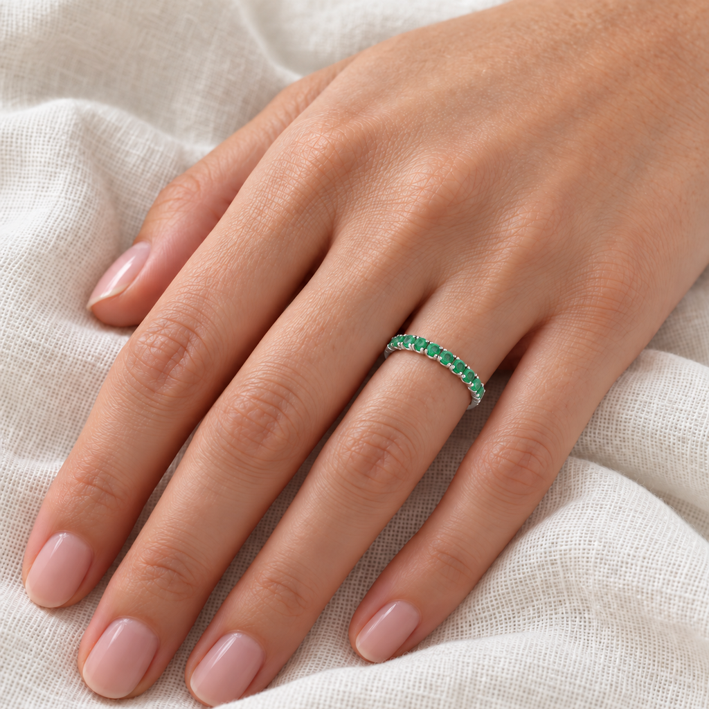 Fine-scale ivory-linen left ring finger view of a high-polished 14k white gold 2.25mm half-eternity ring with seventeen round natural emeralds, 0.95ct