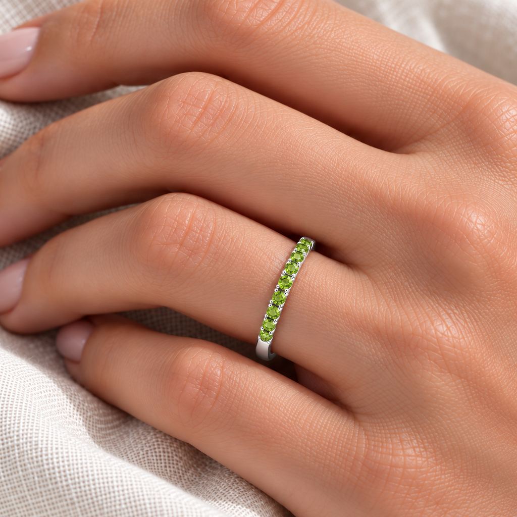 Close ivory-linen hand wearing fine 2 mm half-eternity ring with 19 round faceted natural peridots, 0.65ct, high-polished 14k white gold.