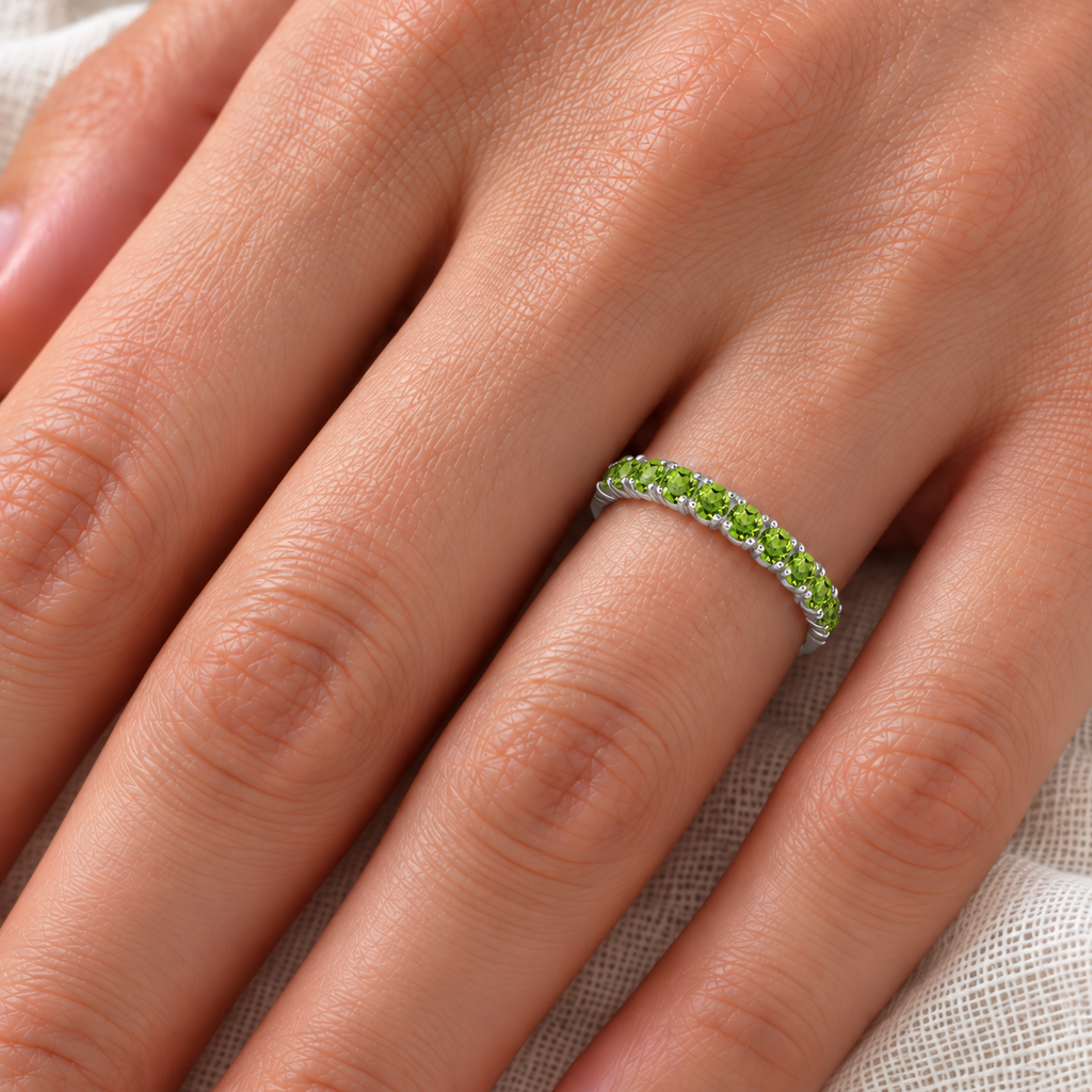 Close ivory-linen hand view of a fine 2.25 mm polished 14k white gold half-eternity pavé ring with 17 round faceted natural peridots, 0.95ct.