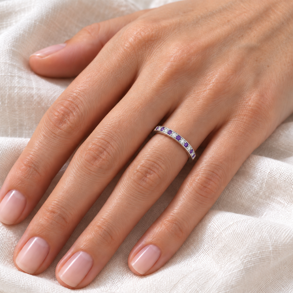 Natural amethyst and diamond channel-set wedding band in palladium on left ring finger, ivory linen closeup