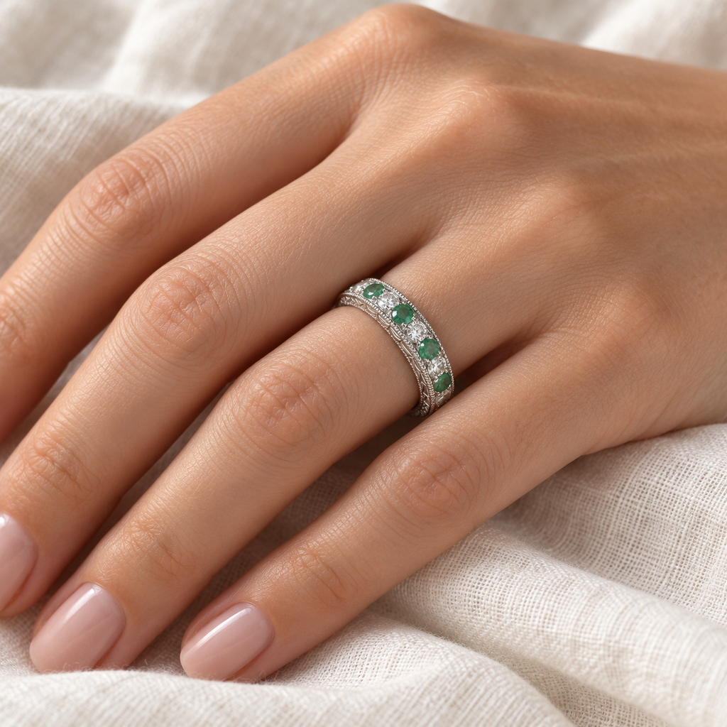 Antique emerald and diamond wedding ring in white gold on left hand against ivory linen