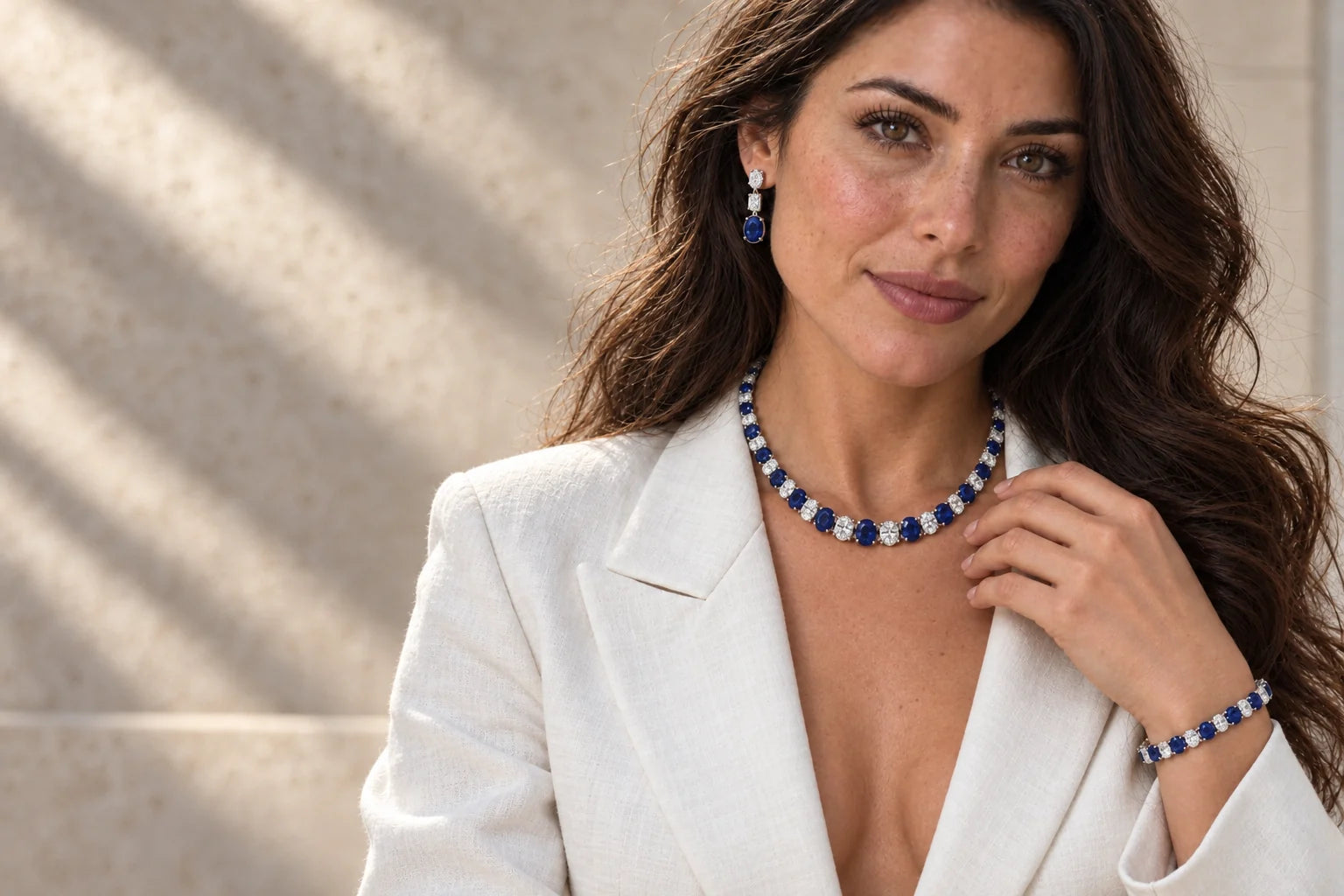 Allurez model in a white blouse wearing a graduated blue sapphire and diamond necklace, small matching drop earrings and a tennis bracelet