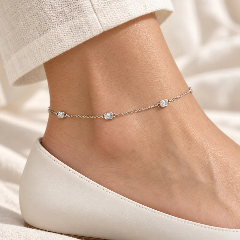 Model wearing a delicate white-gold diamond bezel-station anklet above an ivory shoe